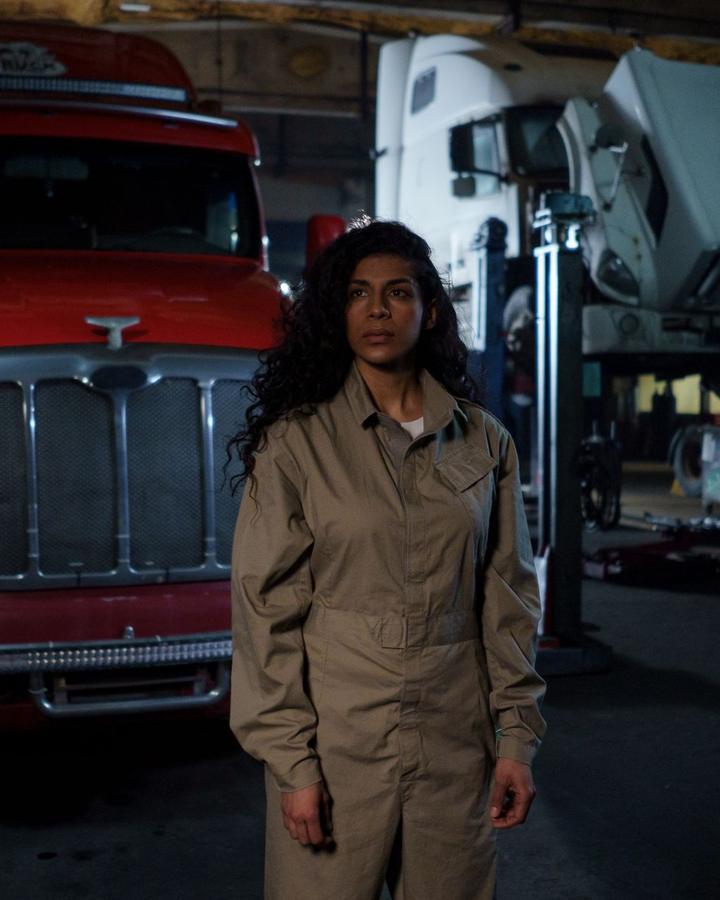 Woman in work coveralls standing in a truck shop next to a red semi