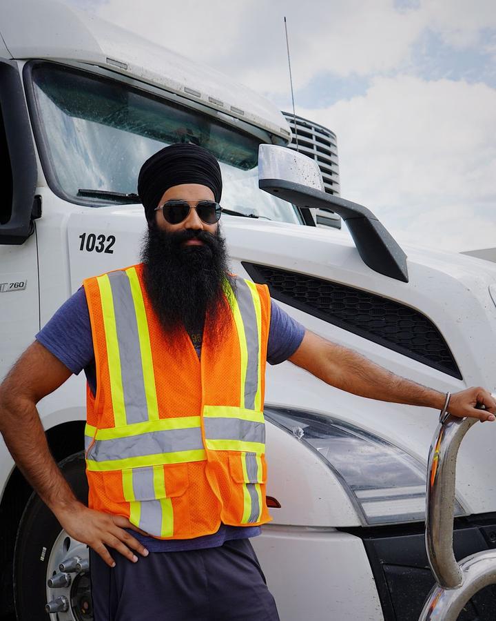 Truck driver in a safety vest standing beside a white semi tractor